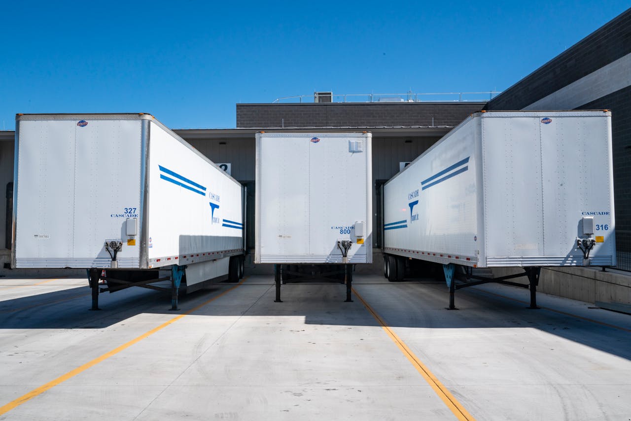 home-img Three white cargo trailers parked at an industrial shipping dock under clear blue skies.